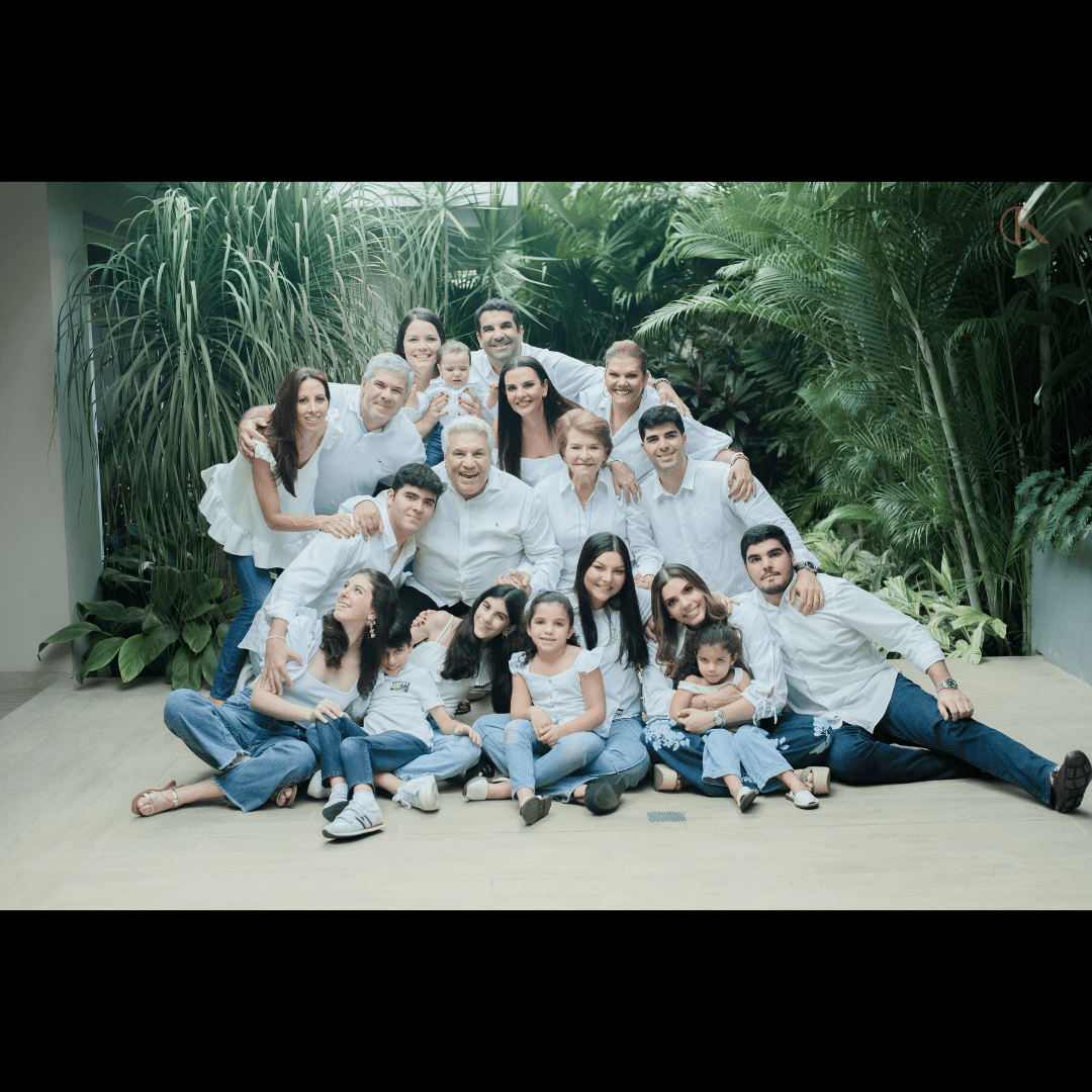 The Altieri family, dressed in white tops and jeans, smiling together while posing outdoors in front of tropical greenery.